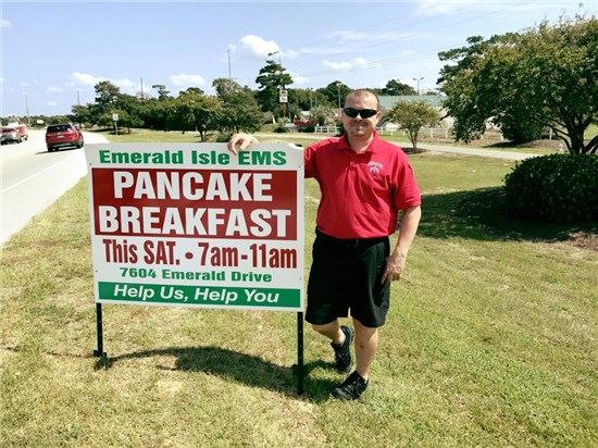 EMS staff member posing by pancake breakfast sign