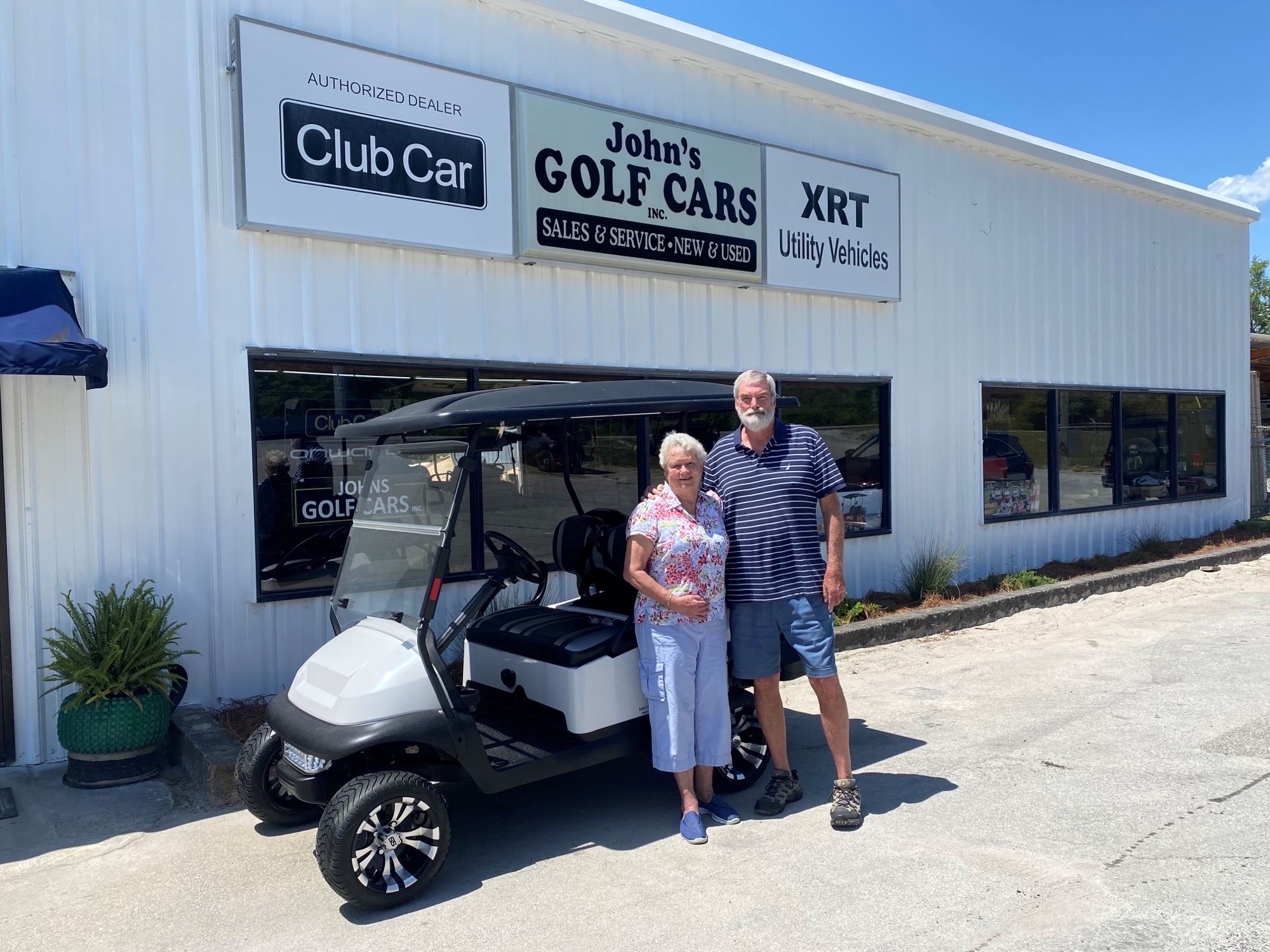 Woman and man stand by a white golf cart in front of a building 