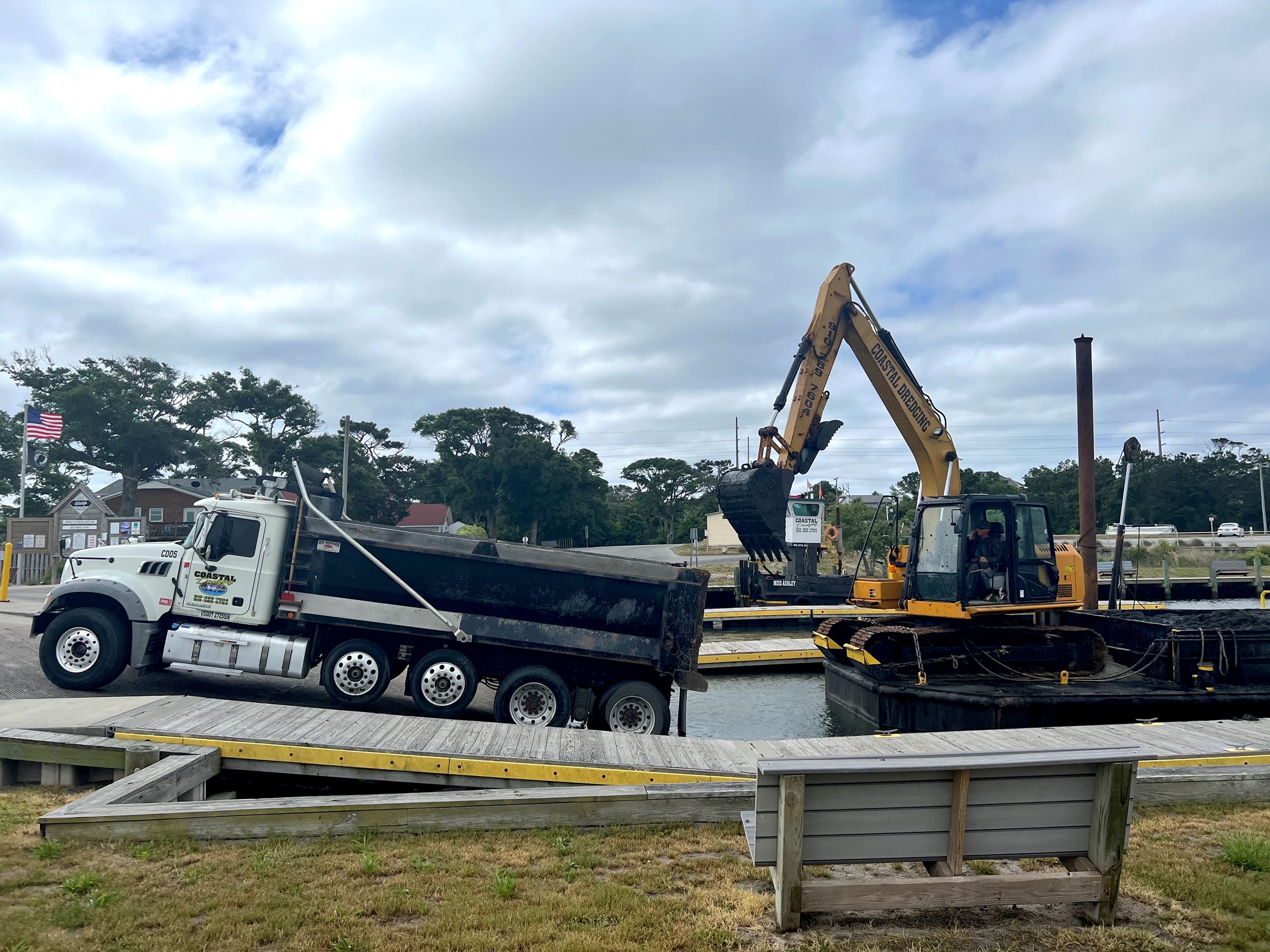 Dredging equipment sits on water by a large dump truck