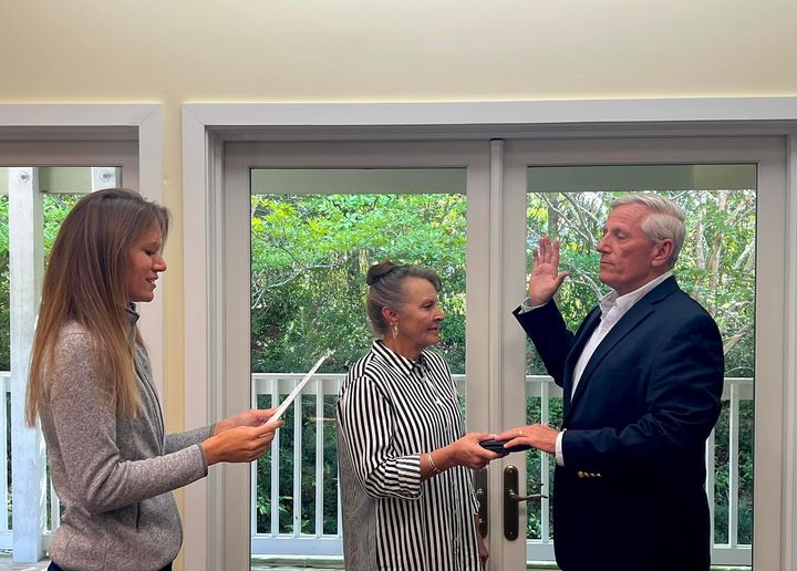 Two women hold a piece of paper and a Bible, while a man has his hands raised and on the Bible