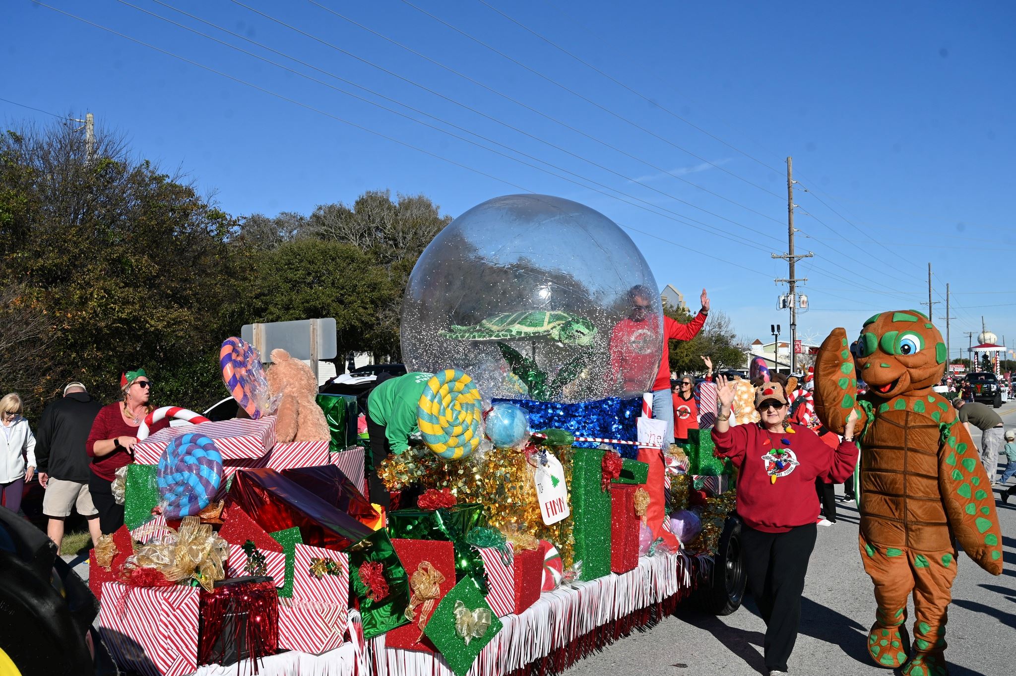 A parade float with wrapped gifts and a snow globe with a sea turtle inside